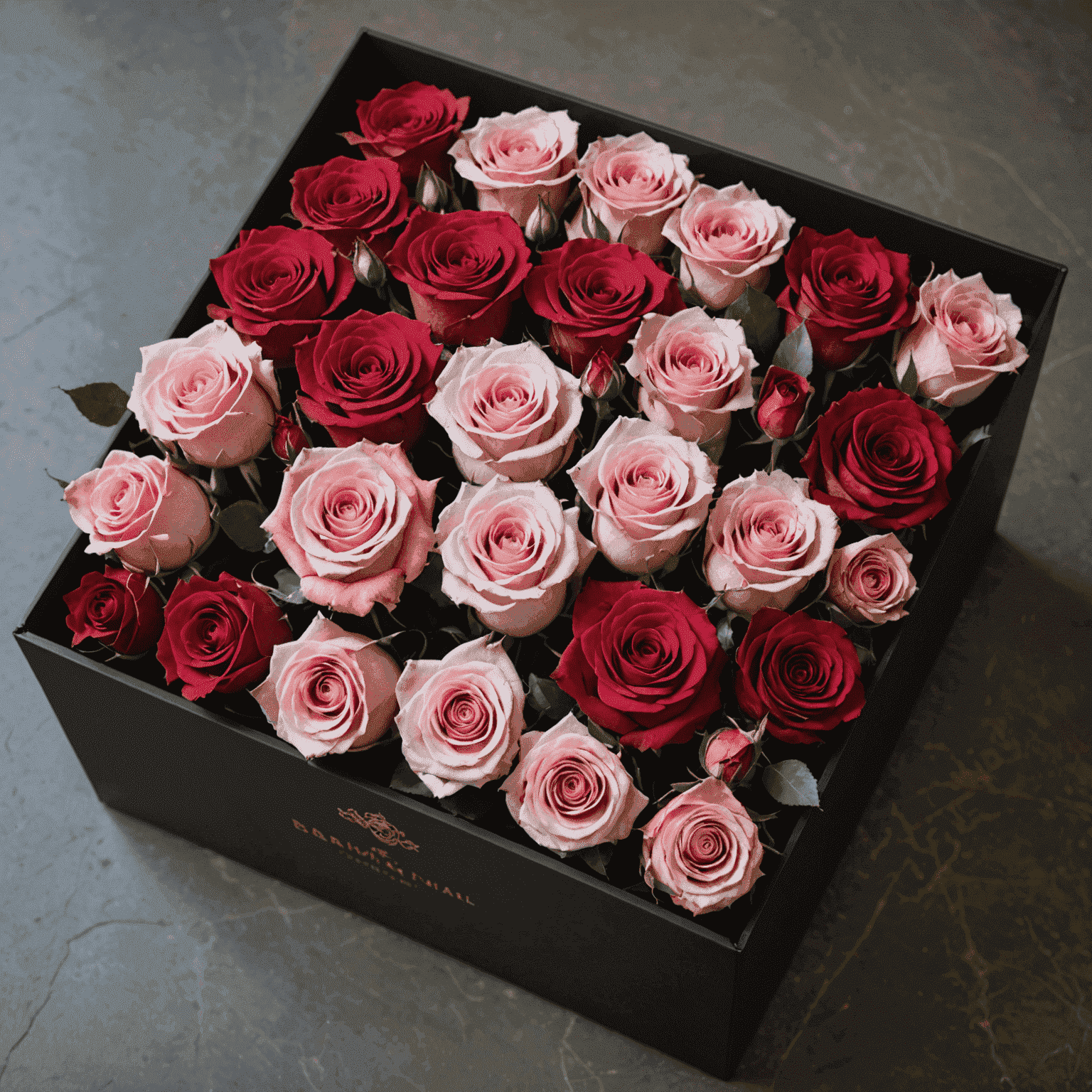An elegant arrangement of preserved roses in various shades of pink and red, displayed in a luxurious black box